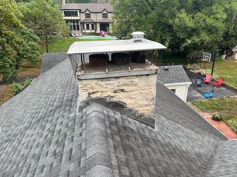 Large stone chimney with a wide metal chase cover on a shingled roof