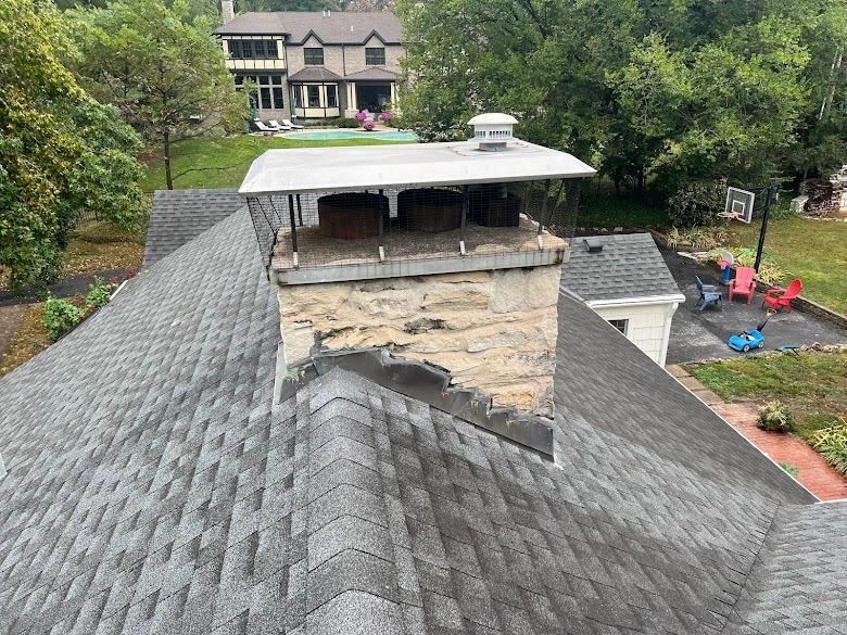 Large stone chimney with a wide metal chase cover on a shingled roof