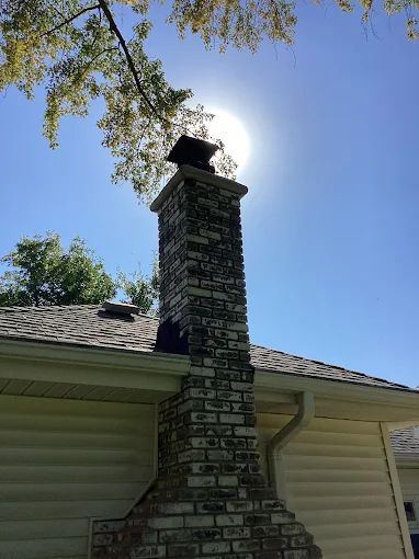 Tall brick chimney rising above a home with the sun behind it