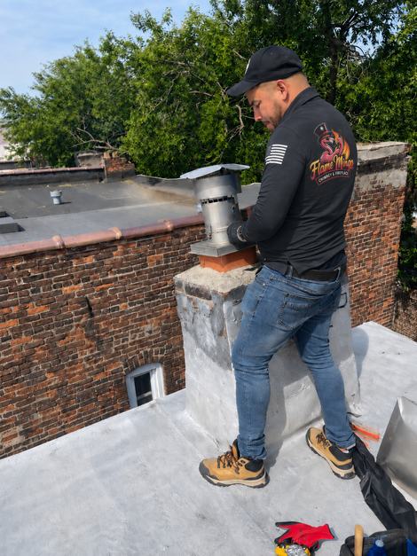 Flame Mingo technician servicing a metal flue and chimney on a flat urban rooftop