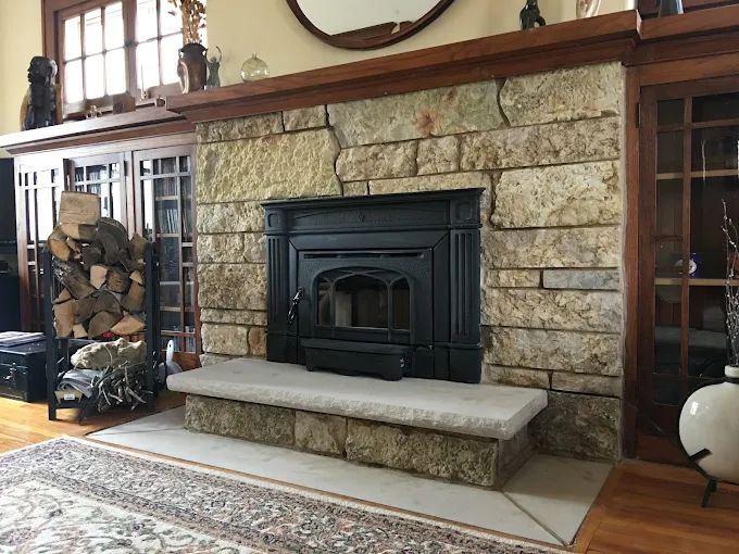 Stone fireplace with a cast-iron wood insert and split firewood stacked beside it