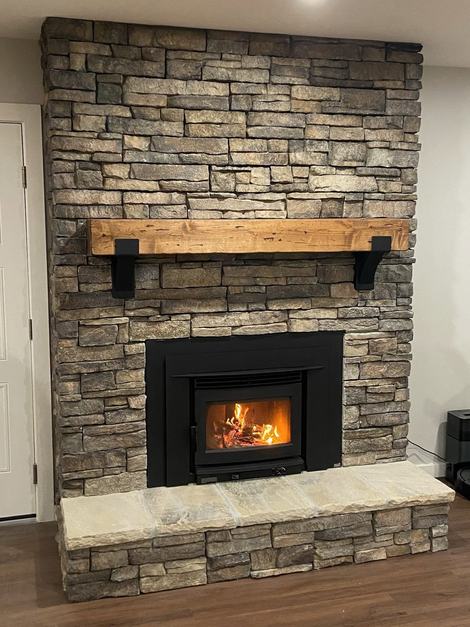 Stacked-stone fireplace with a black wood-burning insert and a reclaimed-wood mantel