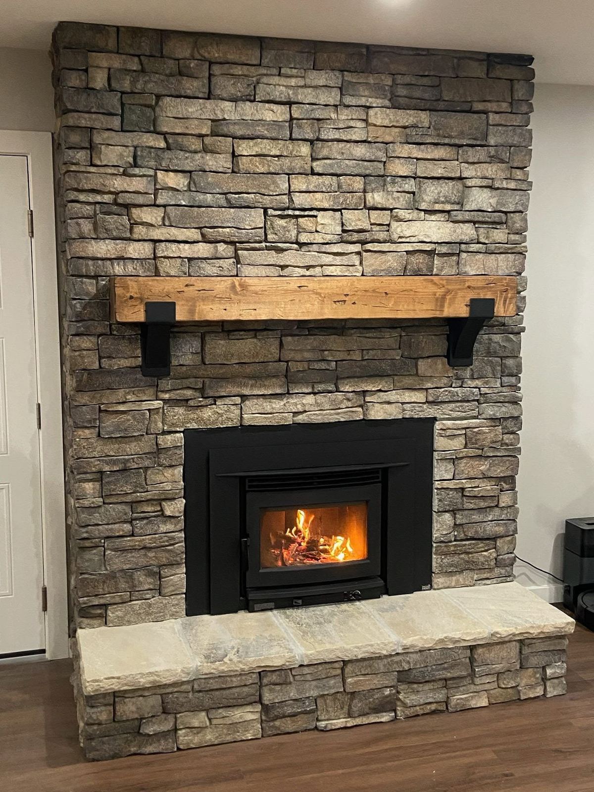 Stacked-stone fireplace with a black wood-burning insert and a reclaimed-wood mantel