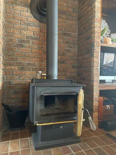 Older wood stove with a brass-trimmed door set against a brick surround